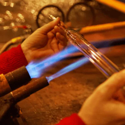 Glassblowing process with hands holding a glass rod over a flame.