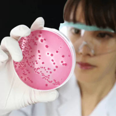 Person in a lab setting holding a petri dish with a pink substance