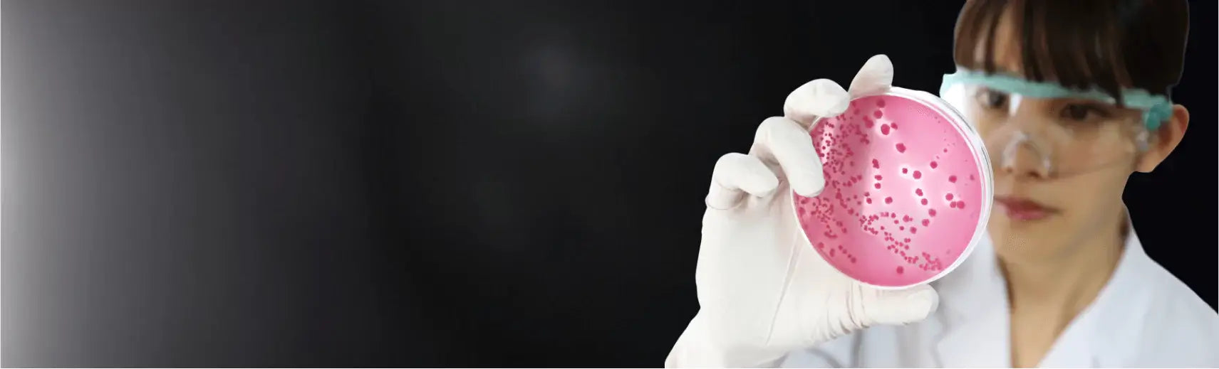 A person in a lab setting holding a Petri dish with a black background