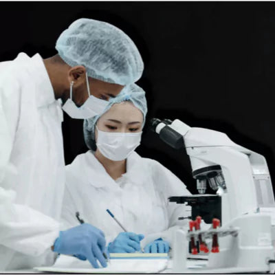 Two scientists in a laboratory setting with a microscope and test tubes.