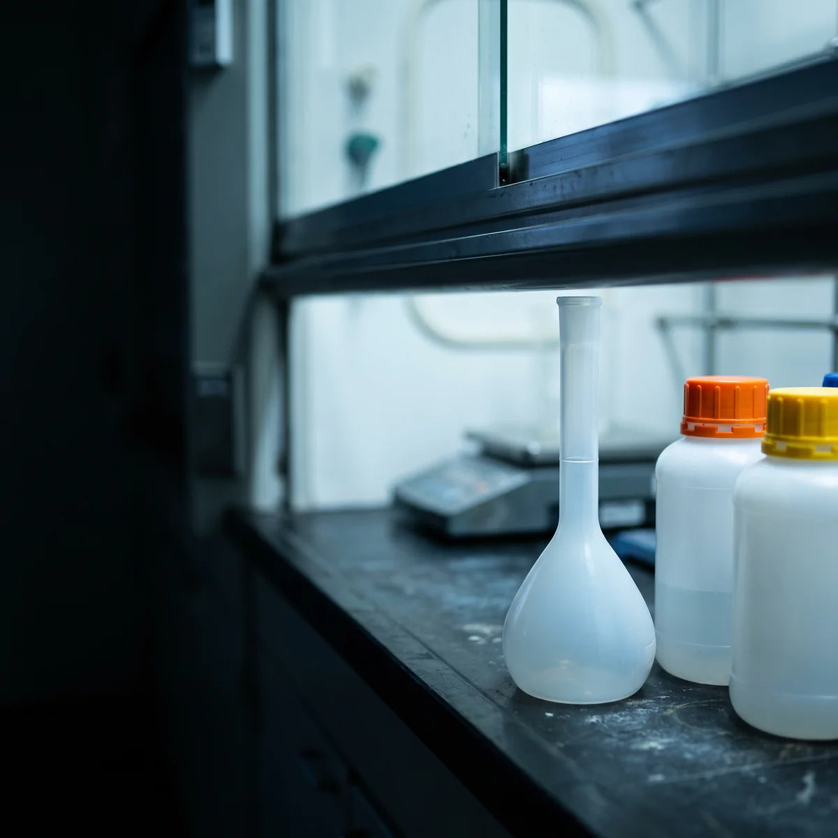 Polypropylene volumetric flask beside sealed reagent bottles of alkali and hydrofluoric acid